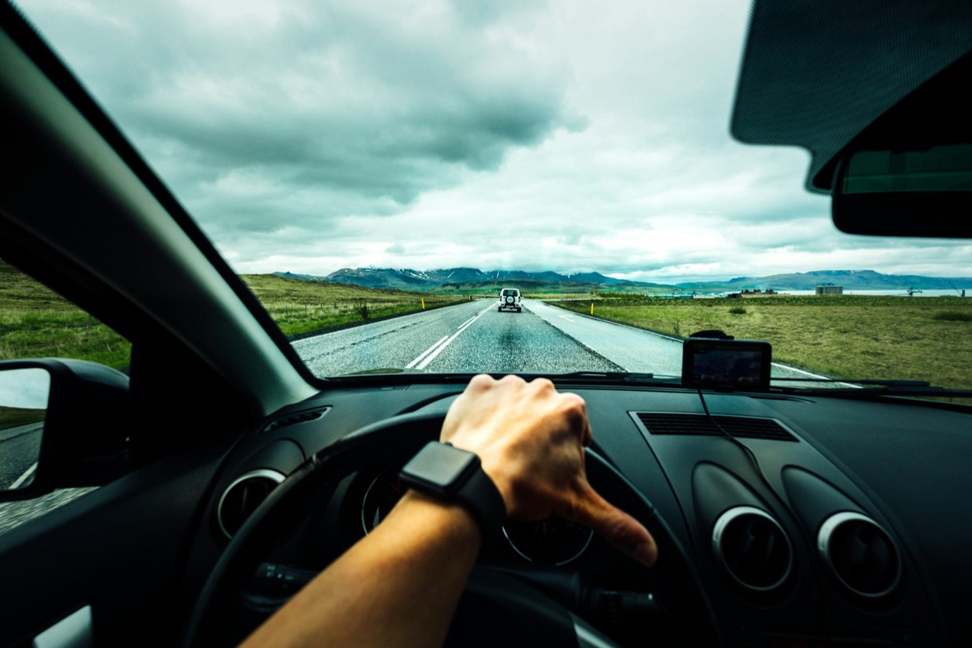 A driver’s hand on the steering wheel on an open road